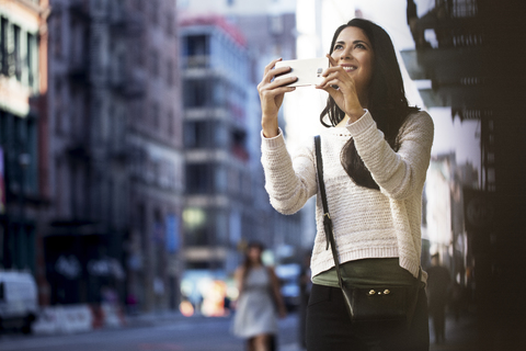 Glückliche Frau fotografiert mit ihrem Smartphone in der Stadt, lizenzfreies Stockfoto