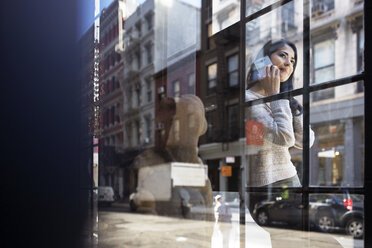 Junge Frau geht durch eine Glaswand hindurch an ihr Smartphone - CAVF32784