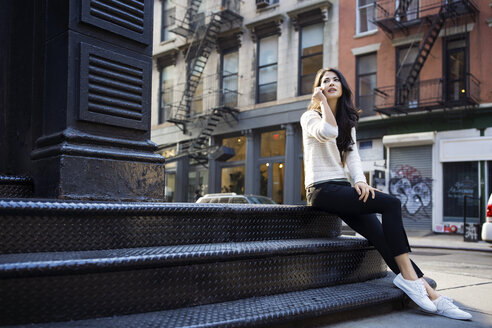 Junge Frau, die ihr Smartphone bedient, während sie auf einer Treppe im Freien sitzt - CAVF32788