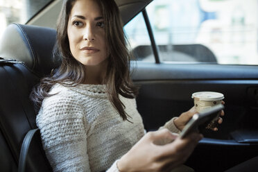 Young woman holding disposable glass and smart phone in taxi - CAVF32795