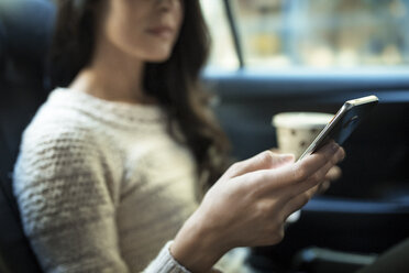 Mittelteil einer Frau, die ein Smartphone benutzt und ein Einwegglas im Taxi hält - CAVF32796