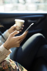 Ausgeschnittenes Bild einer Frau, die ein Smartphone benutzt und ein Einwegglas im Taxi hält - CAVF32799