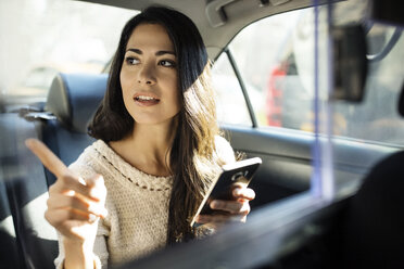 Young woman pointing while holding smart phone in taxi - CAVF32800