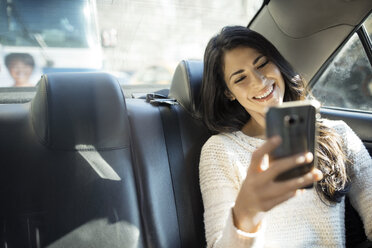 Happy young woman taking selfie through smart phone in taxi - CAVF32801