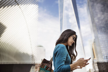 Seitenansicht einer Frau, die ein Smartphone vor dem One World Trade Center benutzt - CAVF32812