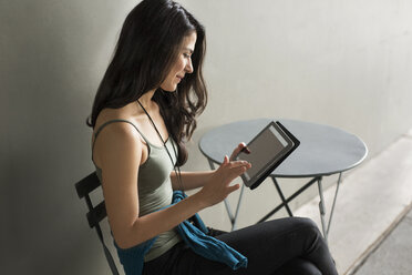 Junge Frau benutzt Tablet-Computer auf einem Stuhl im Freien - CAVF32822