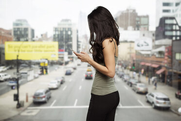 Seitenansicht einer Frau, die ein Smartphone am Glasfenster benutzt, mit einer Straße im Hintergrund - CAVF32828