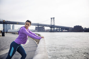 Seitenansicht einer entschlossenen Sportlerin beim Training auf einem Fußweg mit der Williamsburg Bridge im Hintergrund - CAVF32843