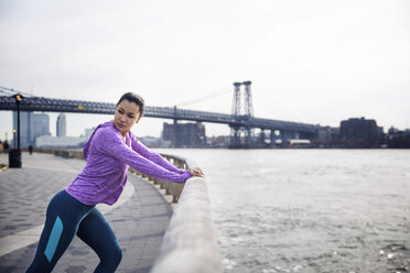 Side view of determined female athlete exercising on footpath with Williamsburg Bridge in background - CAVF32843