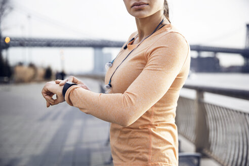 Seitenansicht einer Sportlerin mit Smartwatch auf einem Fußweg mit der Williamsburg Bridge im Hintergrund - CAVF32845