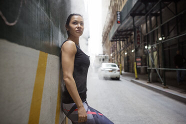 Side view of thoughtful sporty woman leaning on wall by street - CAVF32874