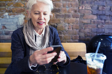 Ältere Frau benutzt ihr Smartphone in einem Straßencafé - CAVF32881