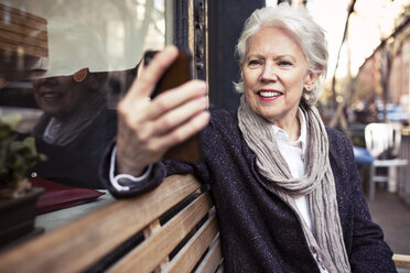 Lächelnde ältere Frau, die ein Smartphone benutzt, während sie auf einer Bank sitzt - CAVF32893