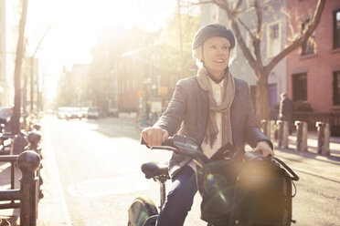 Smiling senior woman sitting on bicycle at street - CAVF32900