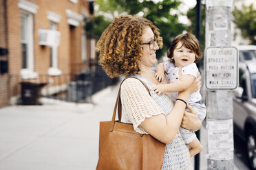 Happy mother holding baby boy while standing on footpath - CAVF32927