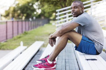 Man looking away while sitting on bleacher at park - CAVF32937