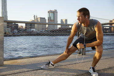 Athlete listening music while exercising on promenade by river - CAVF32955