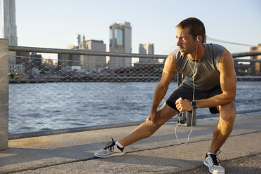 Ein Sportler hört Musik, während er auf der Promenade am Fluss trainiert - CAVF32955