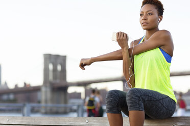 Low angle view of athlete exercising while listening music on bench - CAVF32960