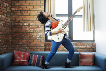 Glückliche Frau singt auf dem Sofa und spielt Gitarre - CAVF33002