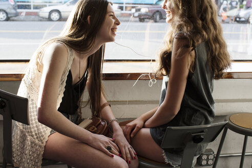 Lächelnde Freundinnen hören Musik, während sie in einem Café sitzen - CAVF33024