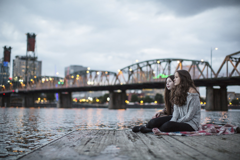 Freundinnen sitzen auf dem Pier vor der Burlington Northern Railroad Bridge 9.6, lizenzfreies Stockfoto