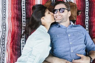 Overhead view of girlfriend kissing boyfriend while lying on blanket in park - CAVF33044