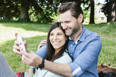 Glückliches Paar nimmt Selfie durch Handy beim Sitzen im Park - CAVF33046