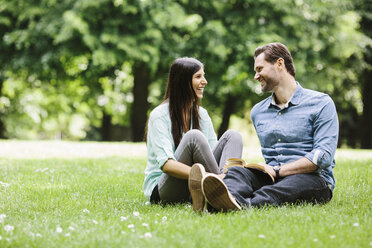 Happy couple looking at each other while relaxing on grassy field in park - CAVF33048