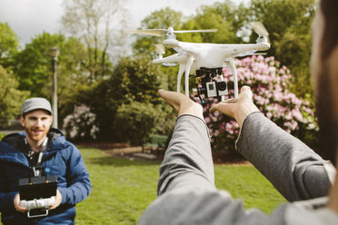 Man operating quadcopter while friend holding it in park - CAVF33058