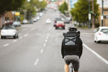 Rear view of male commuter riding bicycle on city street - CAVF33063