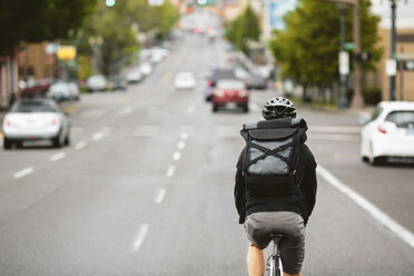 Rückansicht eines männlichen Pendlers, der mit dem Fahrrad auf einer Stadtstraße fährt - CAVF33063