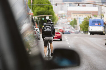 Rückansicht eines männlichen Pendlers mit Rucksack auf dem Fahrrad in der Stadt - CAVF33064