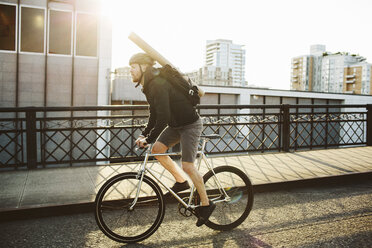 Full length of male commuter with backpack riding bicycle on bridge against sky - CAVF33075