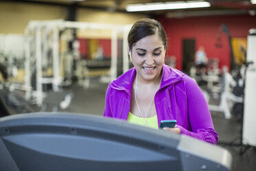 Lächelnde Frau hört Musik, während sie auf dem Laufband im Fitnessstudio trainiert - CAVF33084