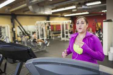 Frau hört Musik, während sie auf dem Laufband im Fitnessstudio trainiert - CAVF33086