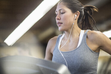 Selbstbewusste Frau hört Musik, während sie auf dem Laufband im Fitnessstudio trainiert - CAVF33089