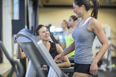 Kursleiter spricht mit einer Frau, die in einem Fitnessstudio auf dem Laufband trainiert - CAVF33092