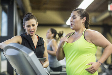 Trainer instruiert Frau beim Training auf dem Laufband im Fitnessstudio - CAVF33093