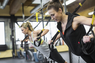 Ausbilderin mit Frau, die mit Widerstandsbändern im Fitnessstudio trainiert - CAVF33096