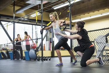 Ausbilderin unterstützt Frau beim Ziehen von Widerstandsbändern im Fitnessstudio - CAVF33098