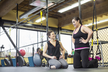 Fitness instructor guiding woman while exercising in gym - CAVF33103