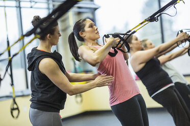 Ausbilder, der Frauen beim Ziehen von Widerstandsbändern im Fitnessstudio hilft - CAVF33105