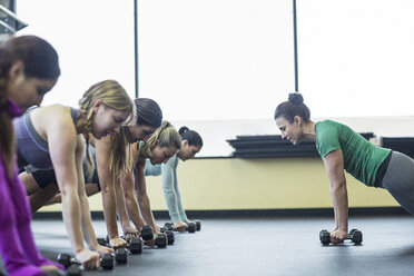 Trainerin leitet Frauen bei Liegestützen mit Hanteln im Fitnessstudio an - CAVF33121