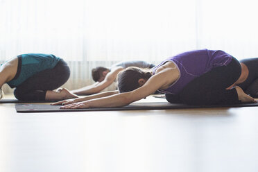 Male instructor with women practicing child's pose in gym - CAVF33156