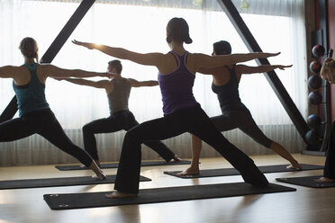 Rear view of male instructor with women practicing warrior pose in gym - CAVF33157