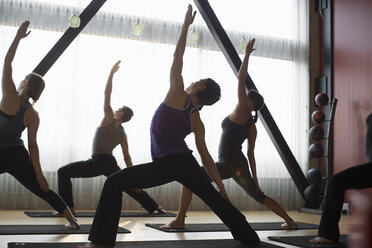 Rückansicht eines männlichen Ausbilders mit Frauen beim Üben der Dreiecksposition im Fitnessstudio - CAVF33161