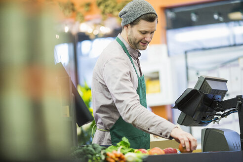 Mann bei der Arbeit, während er an der Kasse eines Supermarktes steht - CAVF33185