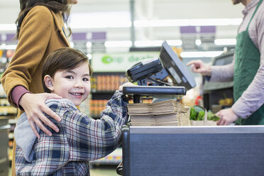 Porträt eines Jungen, der mit seiner Mutter an der Supermarktkasse steht - CAVF33190