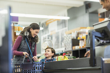 Lächelnde Frau, die einen Korb hält, während sie mit ihrem Sohn im Supermarkt an der Kasse steht - CAVF33193